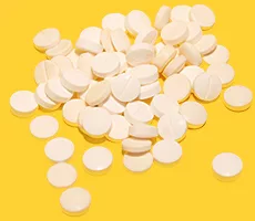 A simple pile of white pills stacked on yellow background